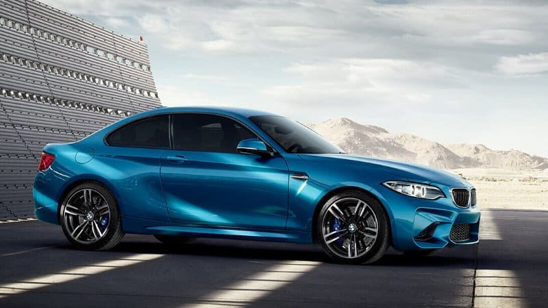 Une voiture de sport bleue garée à l'intérieur à côté d'un mur métallique, avec des montagnes et un ciel partiellement nuageux en arrière-plan - une inspiration parfaite pour toute agence de communication axée sur une image de marque moderne et une esthétique élégante.